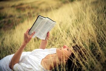 lady reading the Bible while laying on the grass